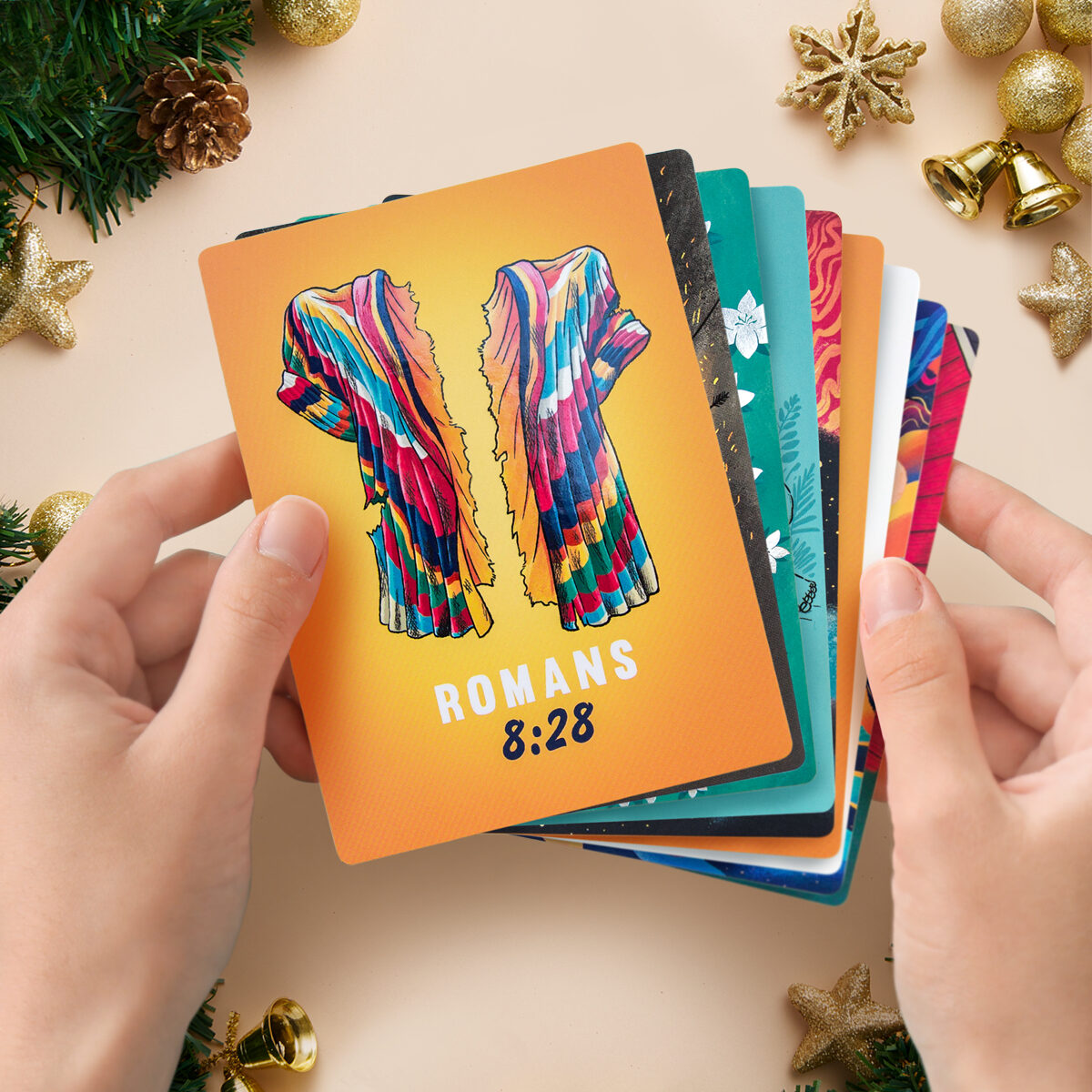 Hand holding a Romans 8:28 illustrated verse card from the Living & Powerful deck, fanned out against other cards